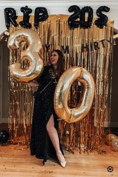 a woman standing in front of a gold balloon number with the number three on it