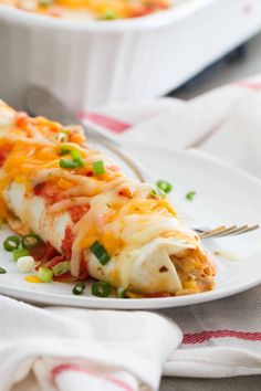 a white plate topped with enchilada covered in cheese and green onions next to a fork