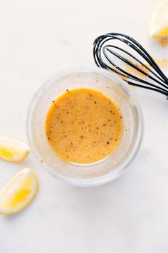 a glass bowl filled with liquid next to some lemons and an whisk