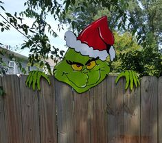 a green griny face with a santa hat peeking over a wooden fence