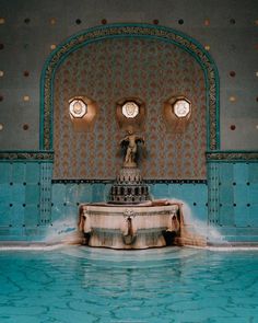 a fountain in the middle of a pool with blue tiles and gold trimmings