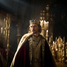 a man in a crown standing next to candles