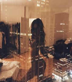 a woman standing in front of a window with city lights behind her and the reflection of buildings