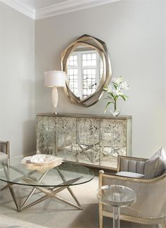 a living room with a glass table and chairs in front of a round mirror on the wall