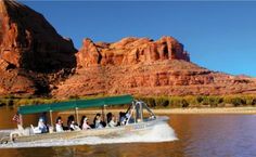 a group of people riding on the back of a boat down a river next to mountains