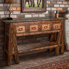 an old wooden table with drawers in front of a brick wall and painting on the wall