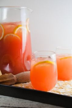 two glasses and pitcher filled with orange juice on a tray next to a wooden spoon