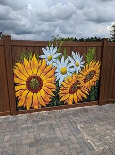 a painted fence with sunflowers and daisies in the center, on top of brick pavers