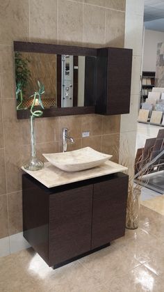 a bathroom sink sitting under a mirror on top of a counter next to a vase with flowers