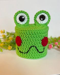 a green crocheted cup with eyes and nose