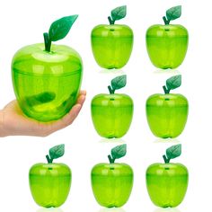 a hand is holding an apple with green leaves on it and eight other apples in the background