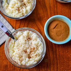 three small glass bowls filled with food on top of a wooden table next to a spoon