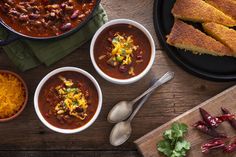 three bowls of chili and bread on a wooden table