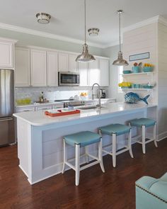 a kitchen with white cabinets and blue stools in front of the island countertop