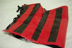 a red and black bag laying on top of a white sheeted bed covered in plastic