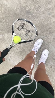 a person holding a tennis racket with a ball on the ground behind them in front of their feet