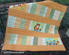 an orange and green baby quilt sitting on top of a black metal bench next to a tree