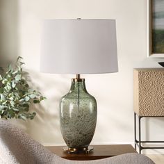 a green vase sitting on top of a wooden table next to a white lampshade