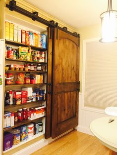 an open pantry door in a kitchen next to a white table and light hanging from the ceiling