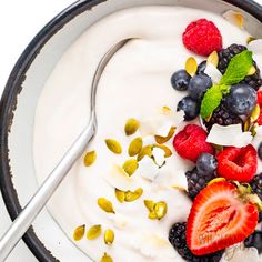 a bowl filled with yogurt, berries and pistachios next to a spoon