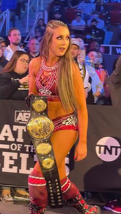 a woman in a wrestling outfit holding a belt and posing for the camera with people watching