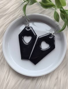 pair of black acrylic earrings on white plate with green plant in the background