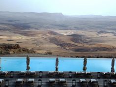 an outdoor pool with chairs and umbrellas in front of the water, overlooking mountains