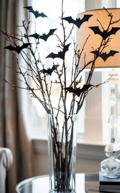 a glass vase filled with branches and bats on top of a table next to a lamp