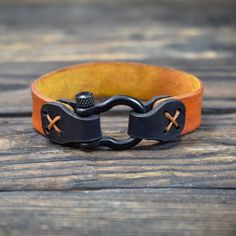 a black and orange leather bracelet with two crosses on the clasp, sitting on a wooden surface