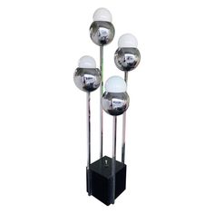 three glass balls are on top of a black stand with four chrome poles and one white ball is in the middle