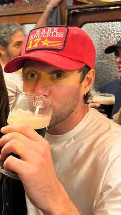 a man wearing a red hat drinking from a wine glass in front of other people