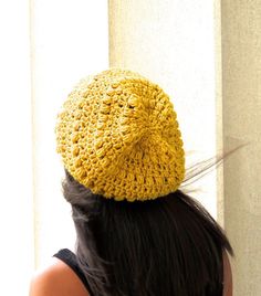 a woman wearing a yellow crochet hat looking out the window with her back to the camera