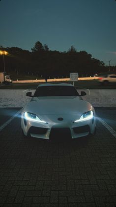 a white sports car parked in a parking lot at night with its headlights turned on