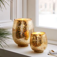 two gold vases sitting on top of a window sill next to a plant