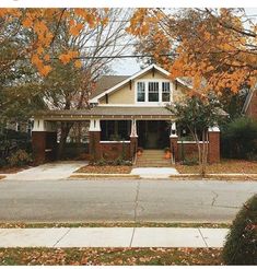 a house with fall leaves on the ground in front of it and trees lining the street