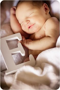 a baby is sleeping next to the letter e with its eyes closed and it's head propped up