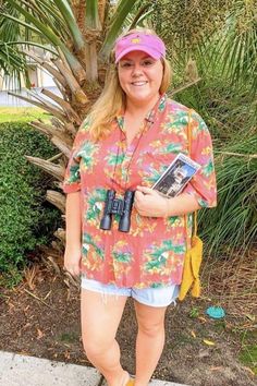 a woman standing in front of a palm tree holding a camera and smiling at the camera