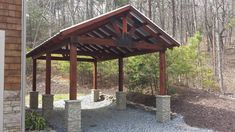 an outdoor covered patio in the middle of a wooded area with rocks and gravel around it