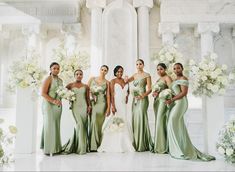 a group of women standing next to each other in front of a white flower covered wall