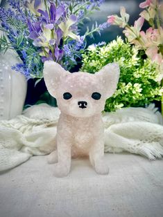 a small white teddy bear sitting on top of a table next to purple and green flowers