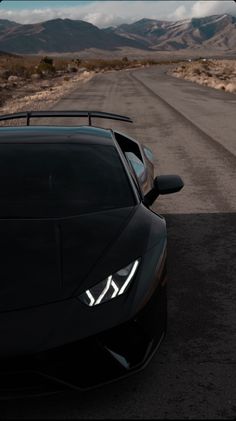 the front end of a black sports car on an empty road with mountains in the background