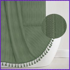 a green shower curtain with white trim and tassels on the bottom, in front of a purple background