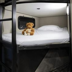 a teddy bear sitting on top of a bunk bed in a room with white sheets