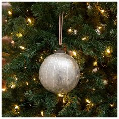 a silver ornament hanging from the top of a christmas tree with lights on it