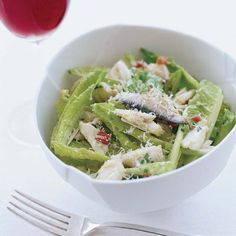 a white bowl filled with salad next to a glass of red wine and a fork