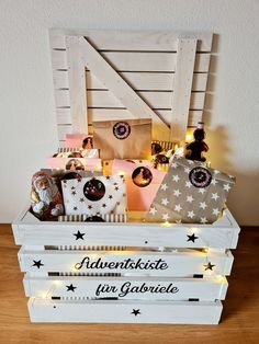 a wooden crate filled with christmas presents on top of a wood floor next to a white wall