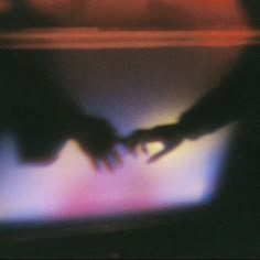 blurry photograph of two hands touching each other's fingers on a television screen