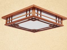 a wooden ceiling light hanging from the side of a beige wall with white glass panels