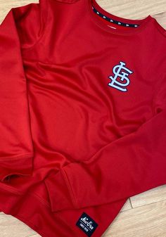 a red long sleeved shirt with the st louis logo on it sitting on a wooden floor