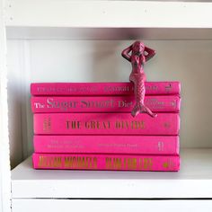 pink books stacked on top of each other with a small figurine in the middle